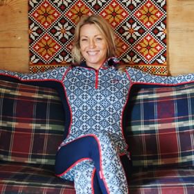 Woman sitting relaxed on a sofa in a patterned room wearing Kari Traa base layer with Nordic design.