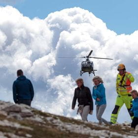 a helicopter flies over several people on a mountain