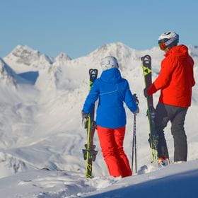 zwei Skifahrer unterhalten sich vor einer Alpenkulisse