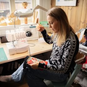 Designer sewing a Scandinavian-style garment in a studio with a Bernina sewing machine.