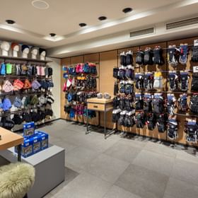 Das Bild zeigt eine Verkaufswand in einem Bründl Sports Shop, auf der verschiedene Handschuhe, Mützen und Accessoires ordentlich ausgestellt sind. Es gibt eine große Auswahl an Winterbekleidung in verschiedenen Farben und Größen