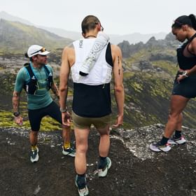 Drei Trailrunner stehen auf einem Berggrat und betrachten die Landschaft während sie Hoka Trailrunning-Schuhe und Laufwesten tragen.