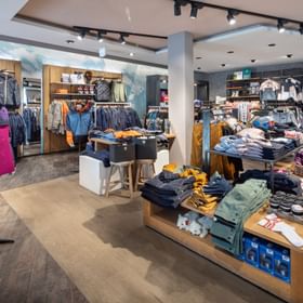 Das Bild zeigt eine Verkaufsfläche eines Bründl Sports Shops mit einer großen Auswahl an Outdoor- und Winterbekleidung. Verschiedene Jacken, Hosen und Accessoires sind auf Regalen und Kleiderständern präsentiert, darunter auch eine farbenfrohe Kollektion von "Peak Performance".