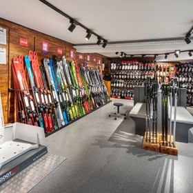 Das Bild zeigt den Innenbereich eines Bründl Sports Shops mit einer großen Auswahl an Skiern, Skischuhen, Stöcken und einem "Bootdoc" 3D-Scanner zur individuellen Skischuhanpassung.