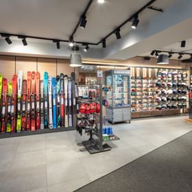 Das Bild zeigt den Verkaufsbereich eines Bründl Sports Shops mit einer großen Auswahl an Skiern, Helmen, Skibrillen und Stöcken. Die Produkte sind übersichtlich an Wänden und auf Ständern präsentiert