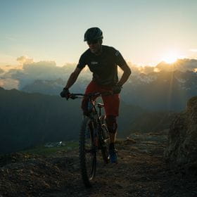 a biker is riding through the mountains while the sun almost set in the background