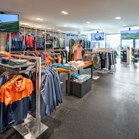 Das Bild zeigt den Innenbereich des Bründl Sports Shops mit Outdoor Bekleidung im Vordergrund. Es gibt Fahrrad T-Shirts zu sehen und Wanderausrüstung.<br/>