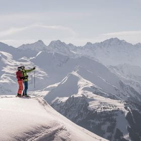 two skiers are standing in the snow and are looking at the distant mountains