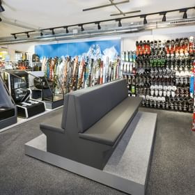 große Sitzbank im Vordergrund, Skischuhe und Ski im Hintergrund <br/>