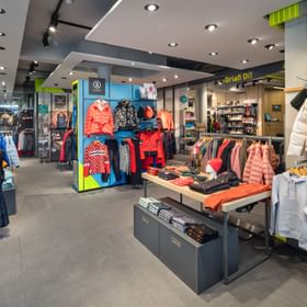 Das Bild zeigt einen Innenbereich eines Bründl Sports Shops, der eine vielfältige Auswahl an Winter- und Outdoor-Bekleidung präsentiert. 