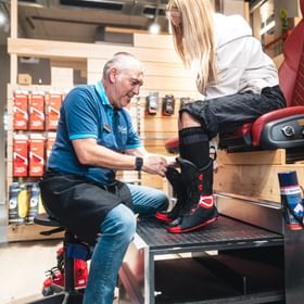 Ein Bründl Sports Mitarbeiter hilft einer Kundin beim Anprobieren des Innenschuhs eines Skischuhs. Die Kundin sitzt auf einem Bootfitting-Sessel, während der Mitarbeiter für die optimale Passform sorgt.