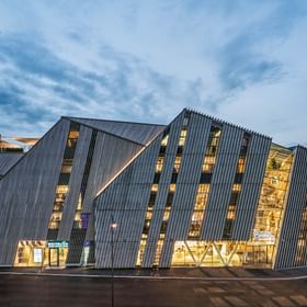 Modern building of the Bründl flagship store with striking glass and wood facade in the Alps, illuminated at dusk.