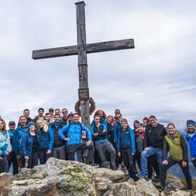 The Bründl Sports employees stand in front of a summit cross.