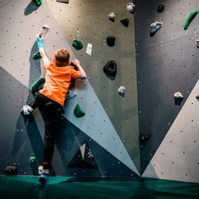 Young boy with an orange shirt while bouldering at the Bründl Sports shop in Saalfelden