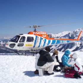 A group of people is sitting on the ground in the background of a helicopter.<br/>