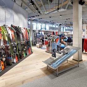 Farbenfrohe Skiwand im Vordergrund, Skizubehör im Hintergrund <br/>