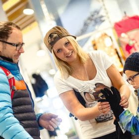 eine junge Verkäuferin hilft einem Kind beim Anprobieren eines Handschuhes