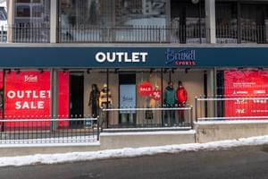 Exterior view of the Bründl Sports Outlet in winter, with large red SALE shop windows and several mannequins dressed in winter sports clothing.