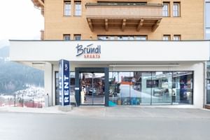 Das Bild zeigt den Eingang eines Bründl Sports Shops in einem alpinen Gebäude. Über dem Eingang befindet sich das Logo, und der Schriftzug "RENT" weist auf die Verleihmöglichkeit hin.