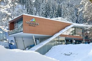 Das Bild zeigt das Bründl Sports Geschäft bei der Talstation der Schmittenbahn in Zell am See, umgeben von verschneiten Bäumen und winterlicher Landschaft. Das Gebäude ist modern und klar gestaltet.