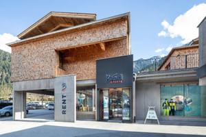 Das Bild zeigt den Eingangsbereich eines Bründl Sports Shops in einem modernen Gebäude mit Holzverkleidung und Glasfronten, umgeben von einer alpinen Landschaft.