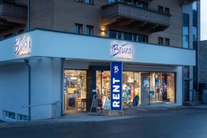 Das Bild zeigt den Eingang eines Bründl Sports Shops in einem alpinen Gebäude. Über dem Eingang befindet sich das Logo, und der Schriftzug "RENT" weist auf die Verleihmöglichkeit hin.
