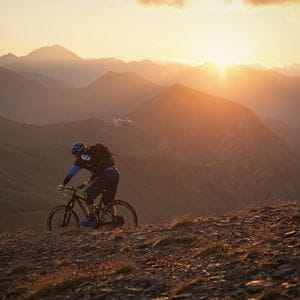 ein Mountainbiker fährt durch die Berglandschaft, während im Hintegrund die Sonne untergeht