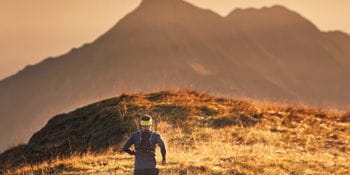 a persons runs through the mountain landscape, in the background the distant mountans coloured in different tones of orange.