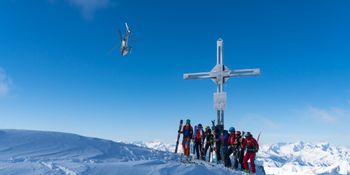 Group picture on a summit while heli-skiing in the background a helicopter.<br/>