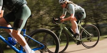 Two road cyclists in green Löffler apparel riding fast on a scenic road