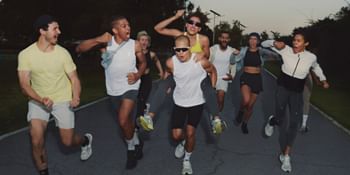 Eine Gruppe sportlich gekleideter Menschen läuft voller Energie und Freude auf einer Straße bei Dämmerung, einige jubelnd und lachend.