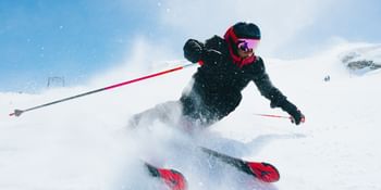 Skier turning in the snow with Atomic Redster skis, snow spraying in the air, blue sky in the background.