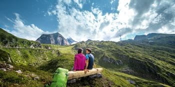 zwei Wanderer sitzen auf einer Bank in der Berglandschaft