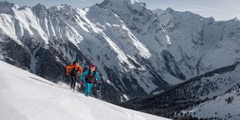 Zwei Personen in Dynafit gekleidet, genießen eine Skitour in winterlicher Landschaft.