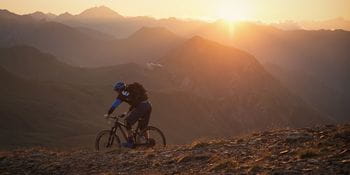 a mountain-biker rides through the mountains while the sun sets