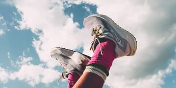 Legs wearing white running shoes and pink sports socks stretch up into a blue sky with clouds.