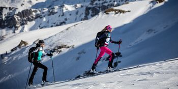 Zwei Frauen gekleidet in Martini beim Skitouren gehen. 