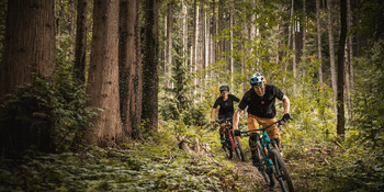 two cyclist riding through the forest dressed in adidas 5.10