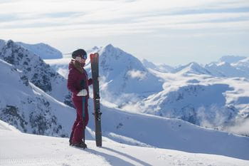 Eine Dame mit einem Paar Rossignol Soul 7 Ski in der Hand genießt das Bergpanorama