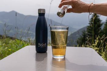isotonisches Getränk im Glas neben der Bründl Sports Thermo-Trinkflasche