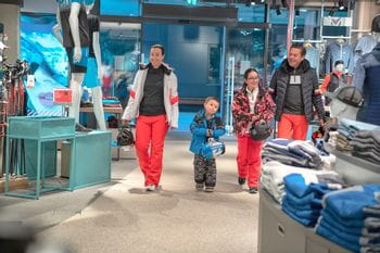 A family dressed in ski clothes enters a sports shop 