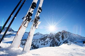 Skier in der Piste steckend, im Hintergrund Berge und die Sonne