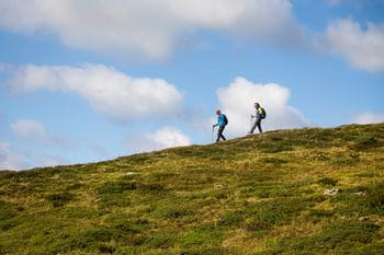 two people are hiking through a mountain landscape with blue clowdy sky in the background