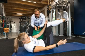 Eine junge Dame bei einer Bauchmuskel Übung unterstützt von Gernot Schweizer