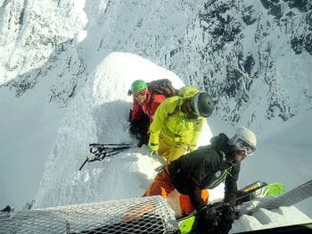 Three men unloading their skiing gear from a helicopter – on a narrow snowy ridge