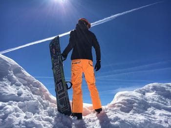 Ein Snowboarder steht im Schnee und blickt in die Ferne.