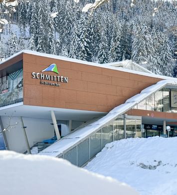 Das Bild zeigt das Bründl Sports Geschäft bei der Talstation der Schmittenbahn in Zell am See, umgeben von verschneiten Bäumen und winterlicher Landschaft. Das Gebäude ist modern und klar gestaltet.