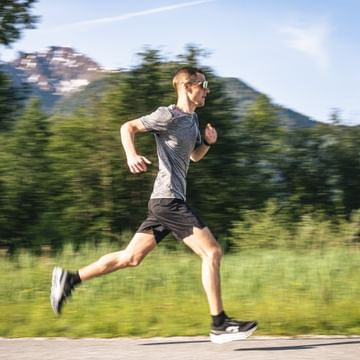 Runner runs in side view on a paved path through a green alpine landscape.