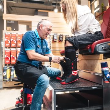 A Bründl Sports employee assists a customer in trying on the inner liner of a ski boot. The customer sits on a bootfitting chair while the employee ensures the perfect fit.