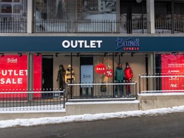Exterior view of the Bründl Sports Outlet in winter, with large red SALE shop windows and several mannequins dressed in winter sports clothing.